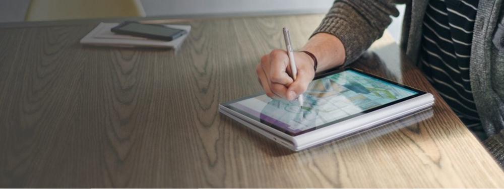 A photograph of someone using a Microsoft Surface device with a stylus in tablet orientation.