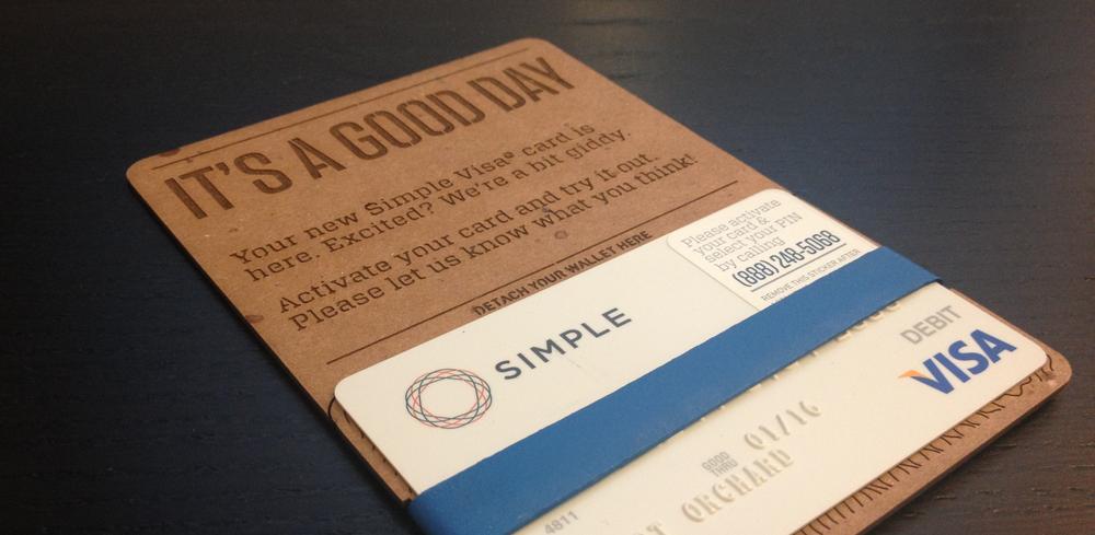 Photograph of a Simple bank debit card package, strapped to a cardboard mailer reading “it’s a good day.”